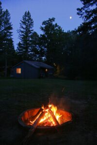 Campfire with cabin in background in the woods
